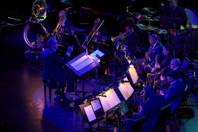 Andy Farber conducting the orchestra with dramatic blue and purple lighting